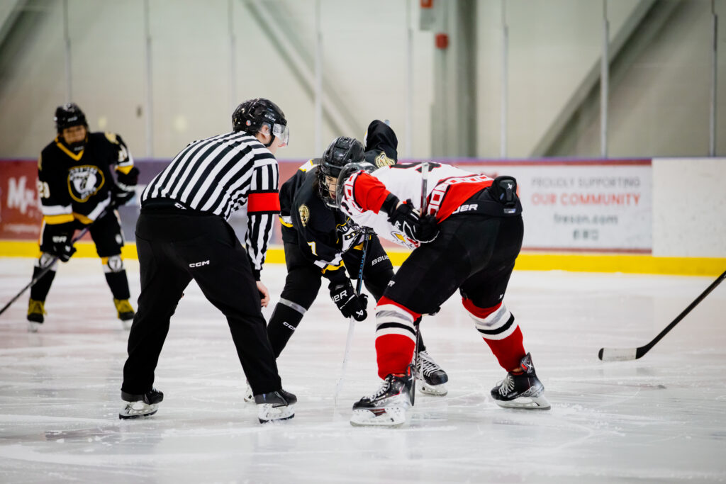 Hockey players face off next to a ref.
