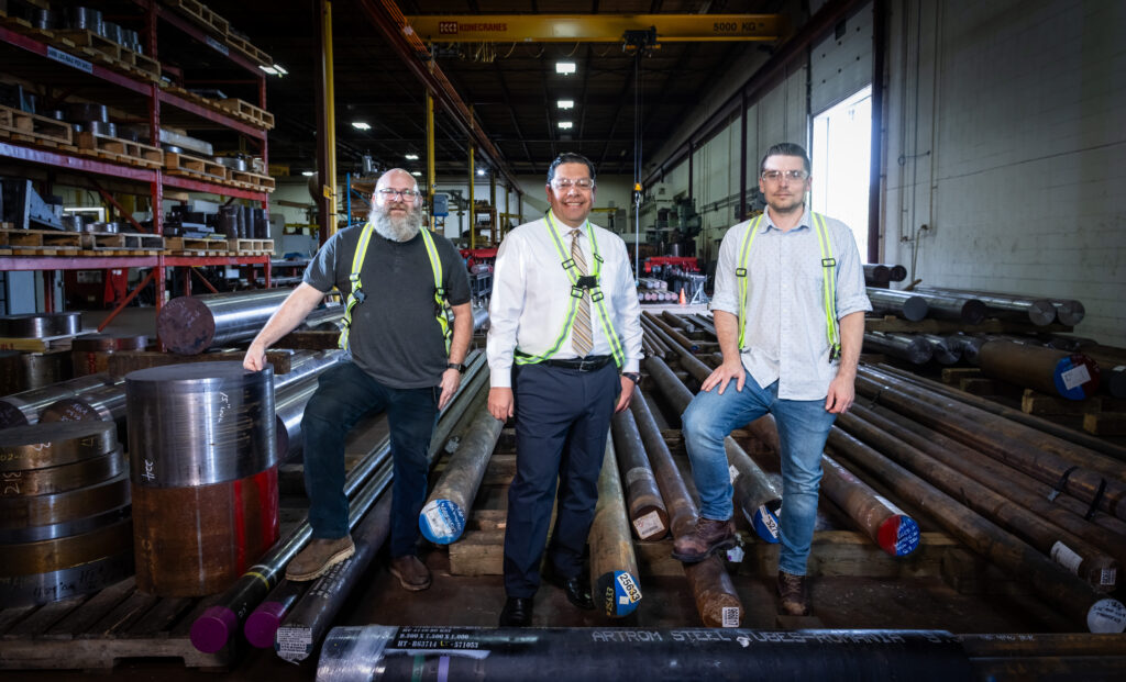 Three men stand side-by-side in a machine shop.